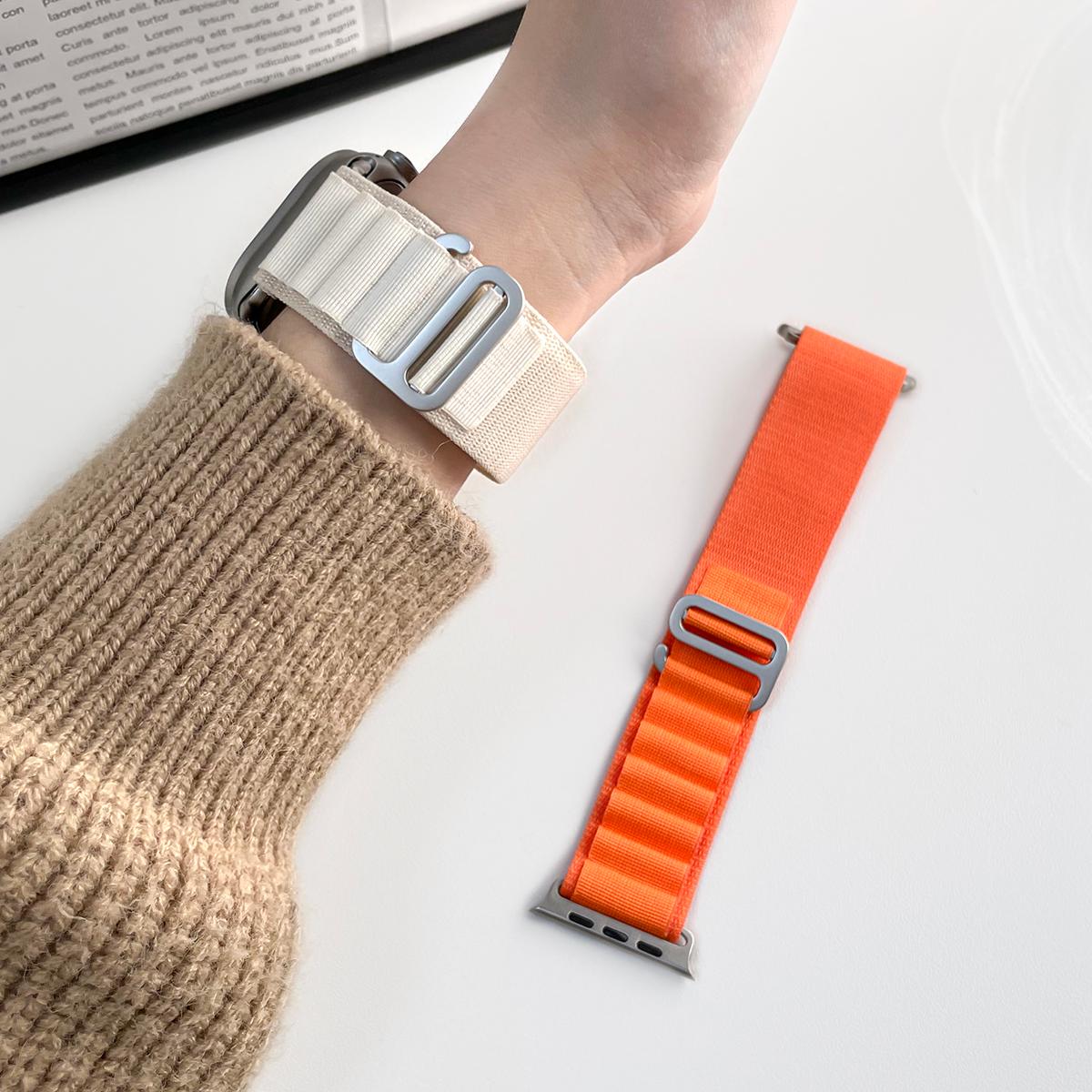 Pearl White Alpine Loop nylon Apple Watch band worn on the wrist with an orange band beside it